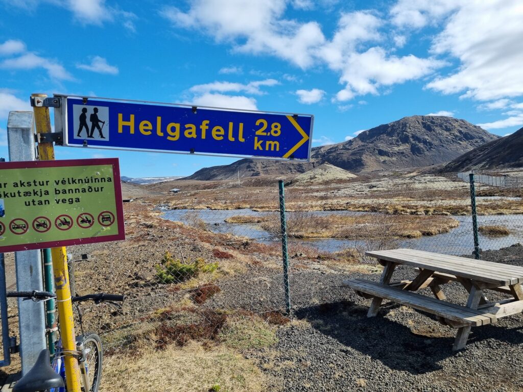Skilti sem bendir á Helgafell. Helgafell í Hafnarfirði í bakgrunni.